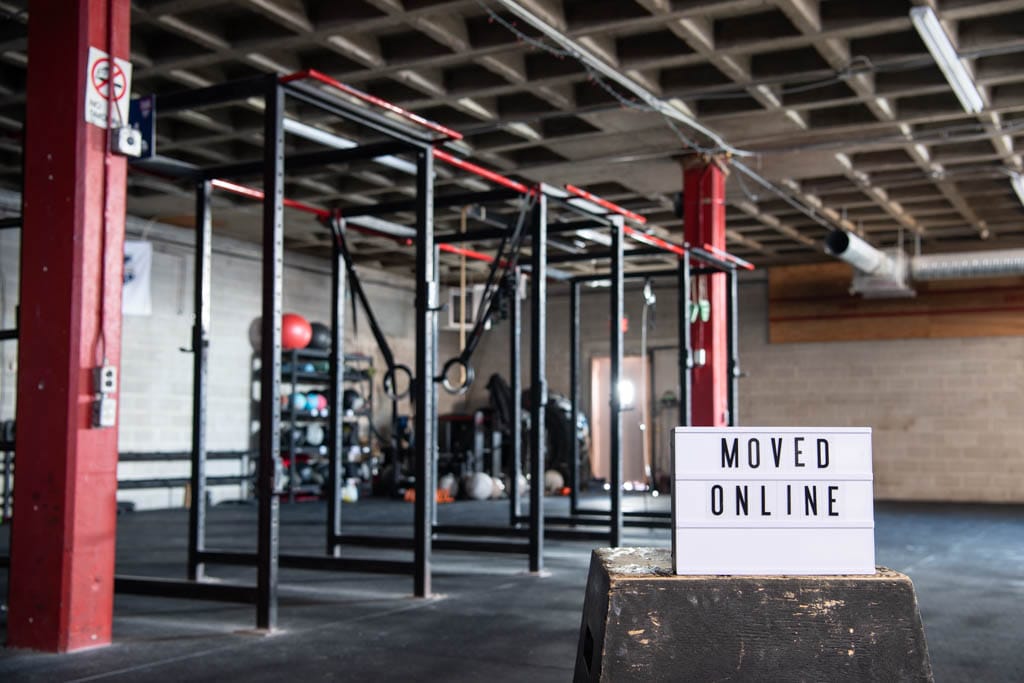 The interior of a sunlit CrossFit gym with a sign that reads "moved online" during the coronavirus crisis.