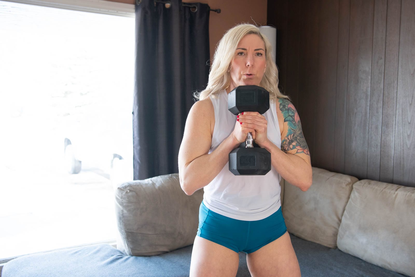 A blond woman holds a dumbbell in her living room as she performs an online workout in Winnipeg.