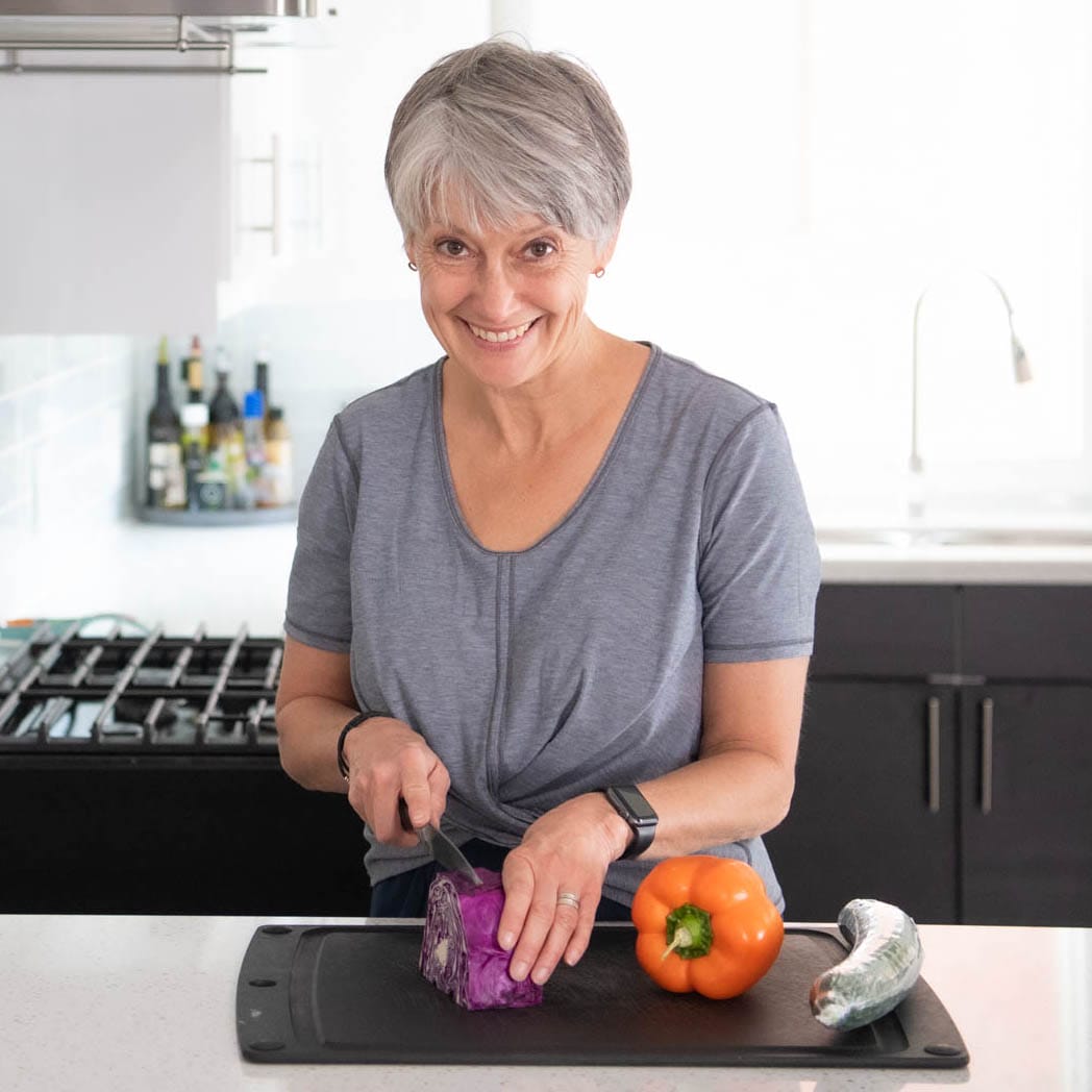A nutrition coach chops brightly coloured vegetables in her kitchen.
