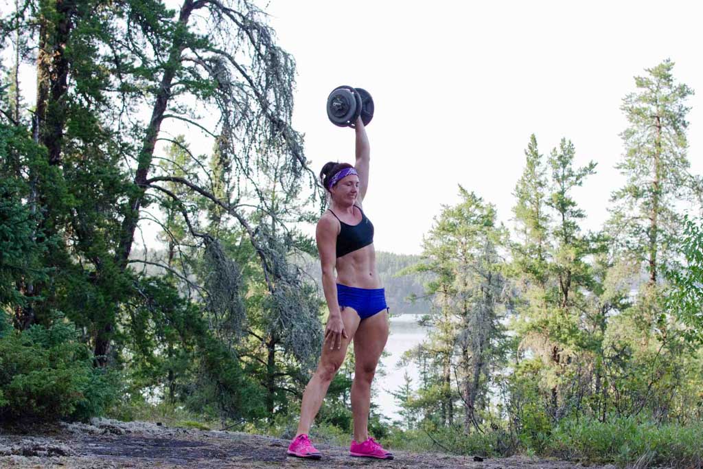 A fit woman performs an online fitness workout with a dumbbell at Rushing River near Kenora.